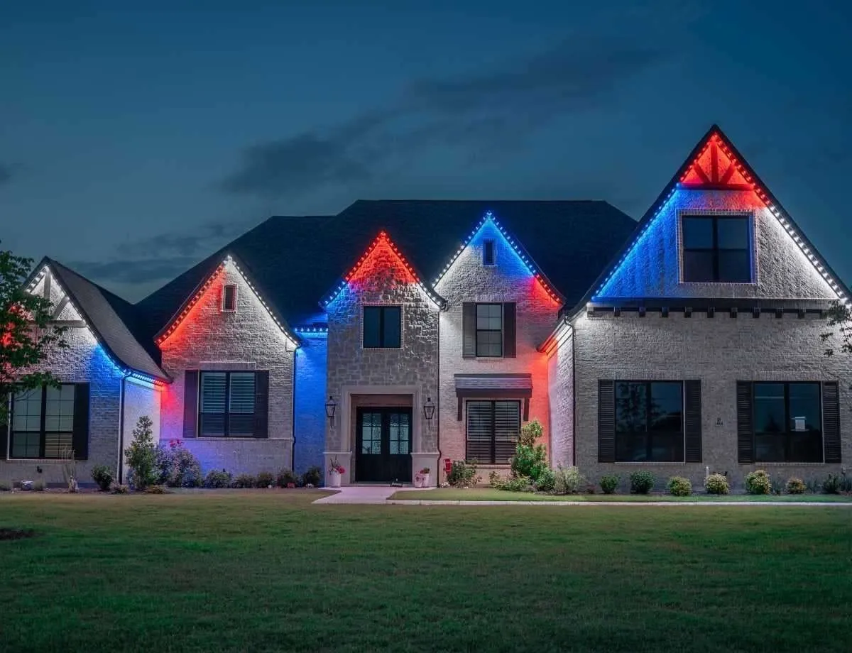 Stone home at dusk with red, white and blue lights along every gable and roof edge.