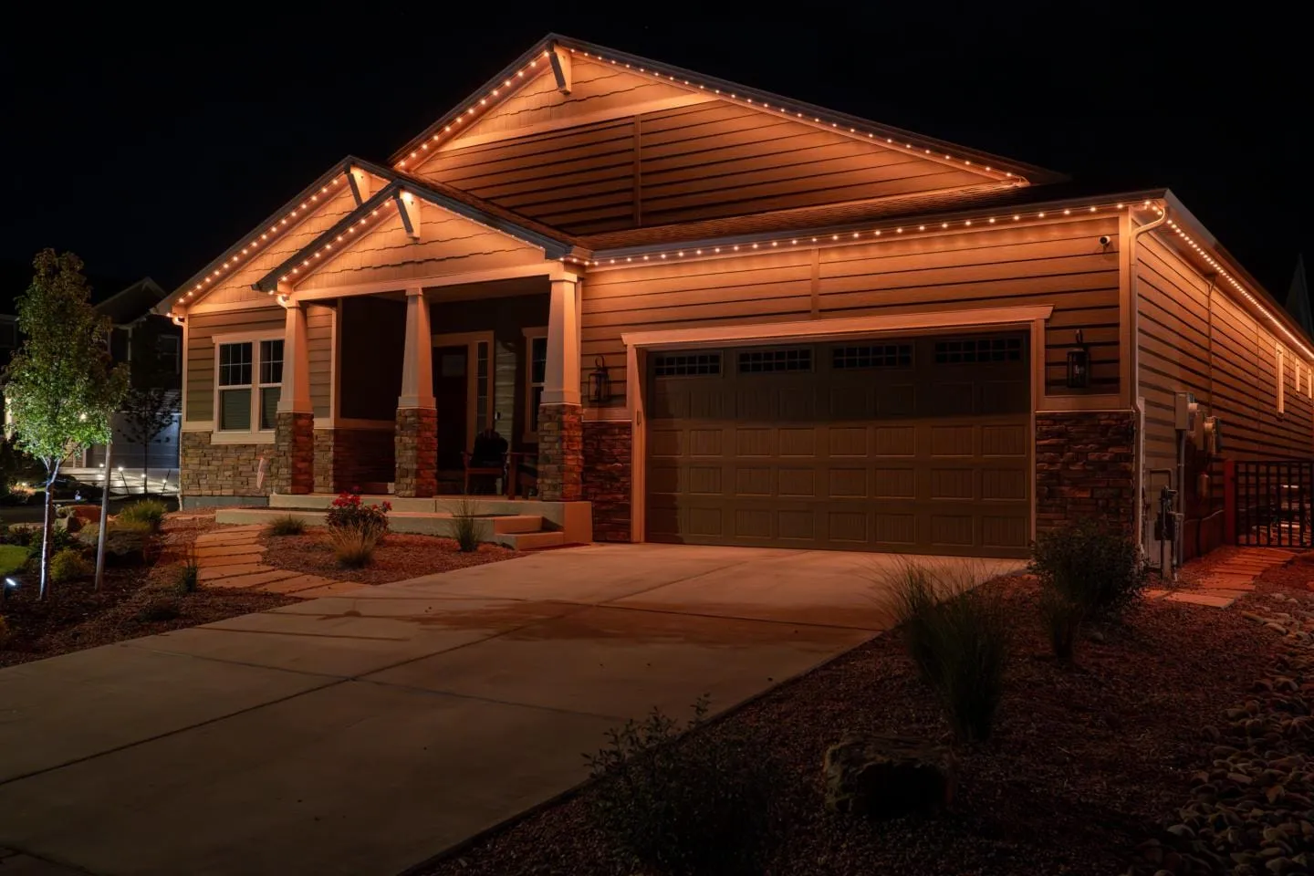 Craftsman style home at night with warm white lights outlining the roofline, gables and garage.